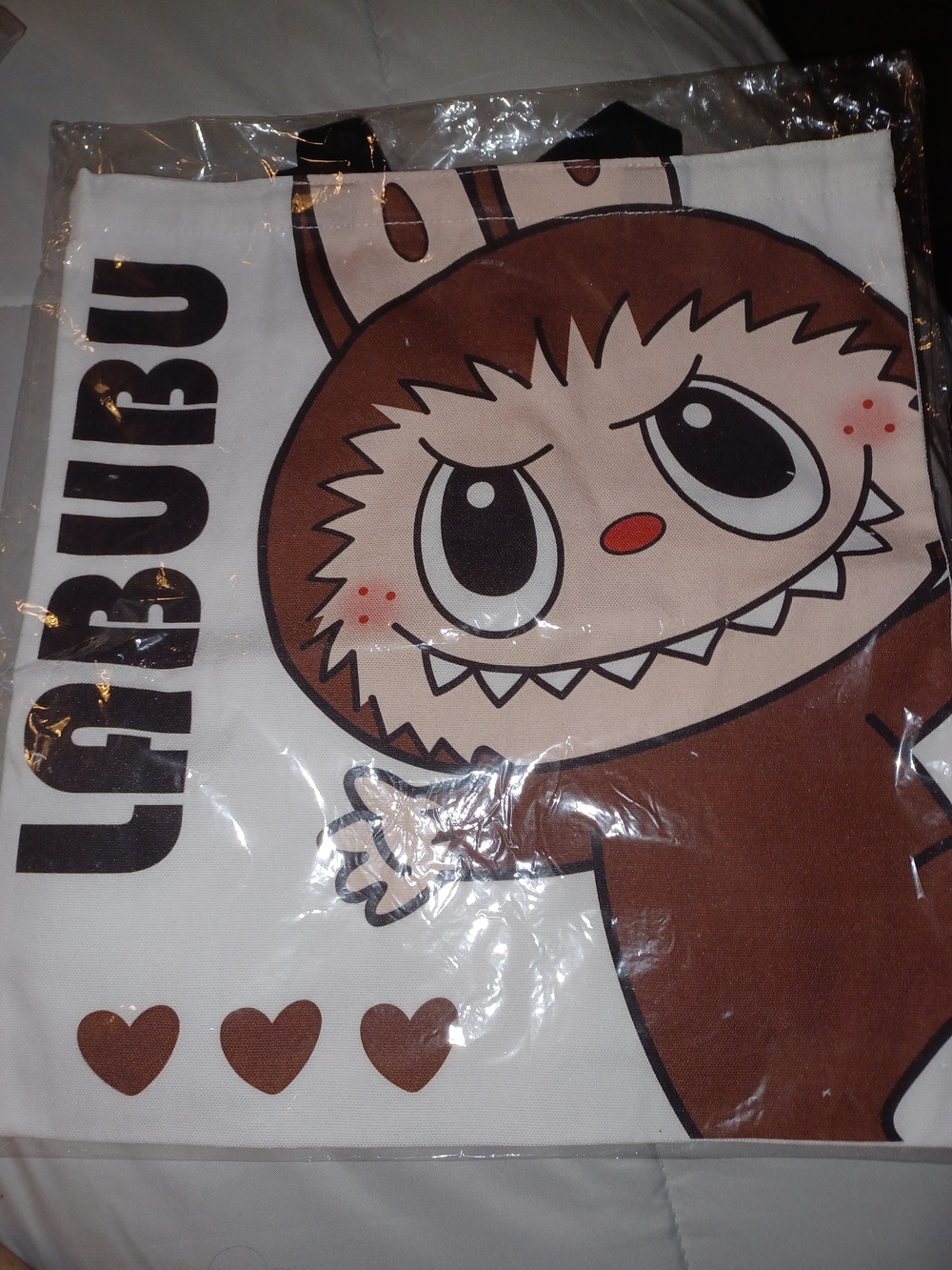 White canvas tote bag featuring a brown Labubu monster graphic and bold vertical